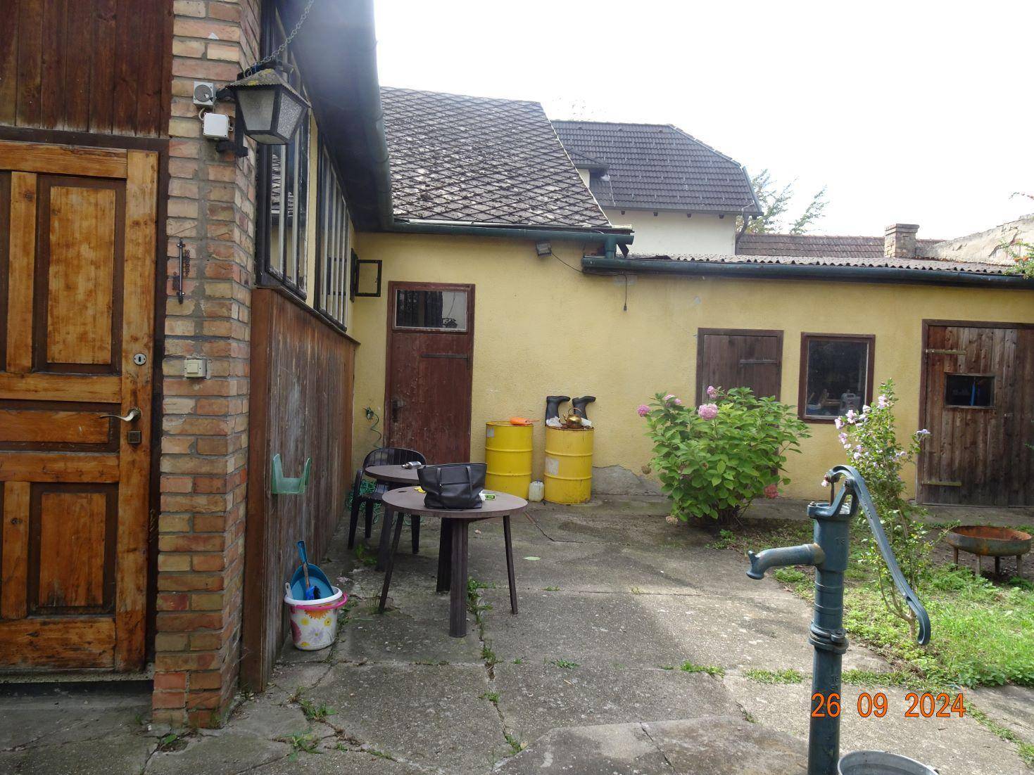 Kleiner gepflasterter Bereich mit Gartentisch und Stühlen neben dem gelben Nebengebäude.