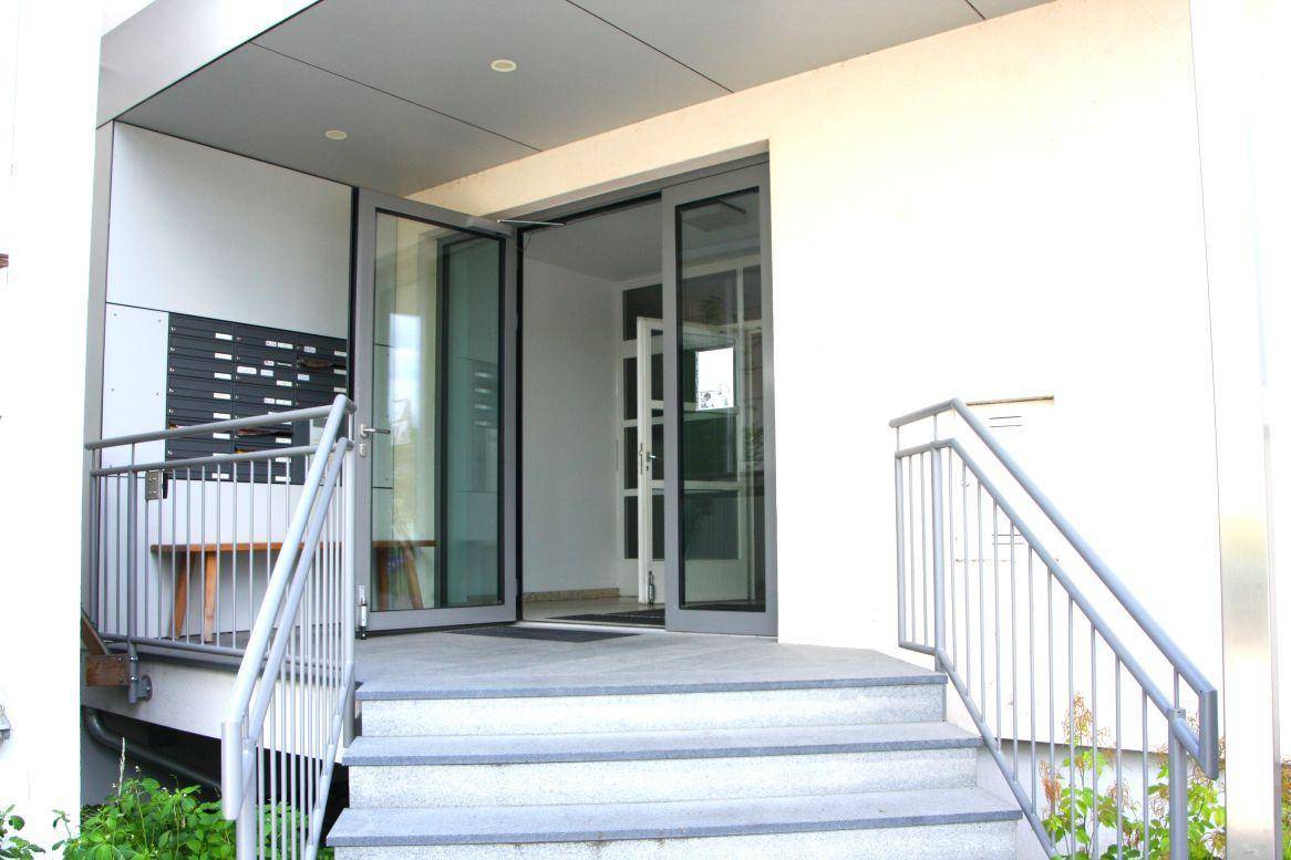 Moderner Eingangsbereich eines Mehrfamilienhauses mit Treppe und Briefkästen.