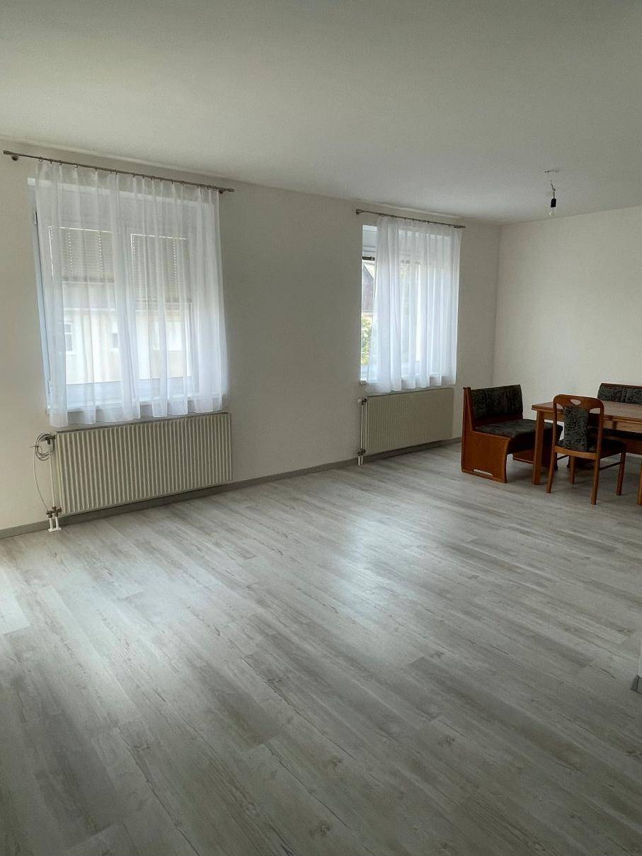 Geräumiger Wohn- und Essbereich mit hellem Laminatboden und viel Tageslicht durch die Fenster.
