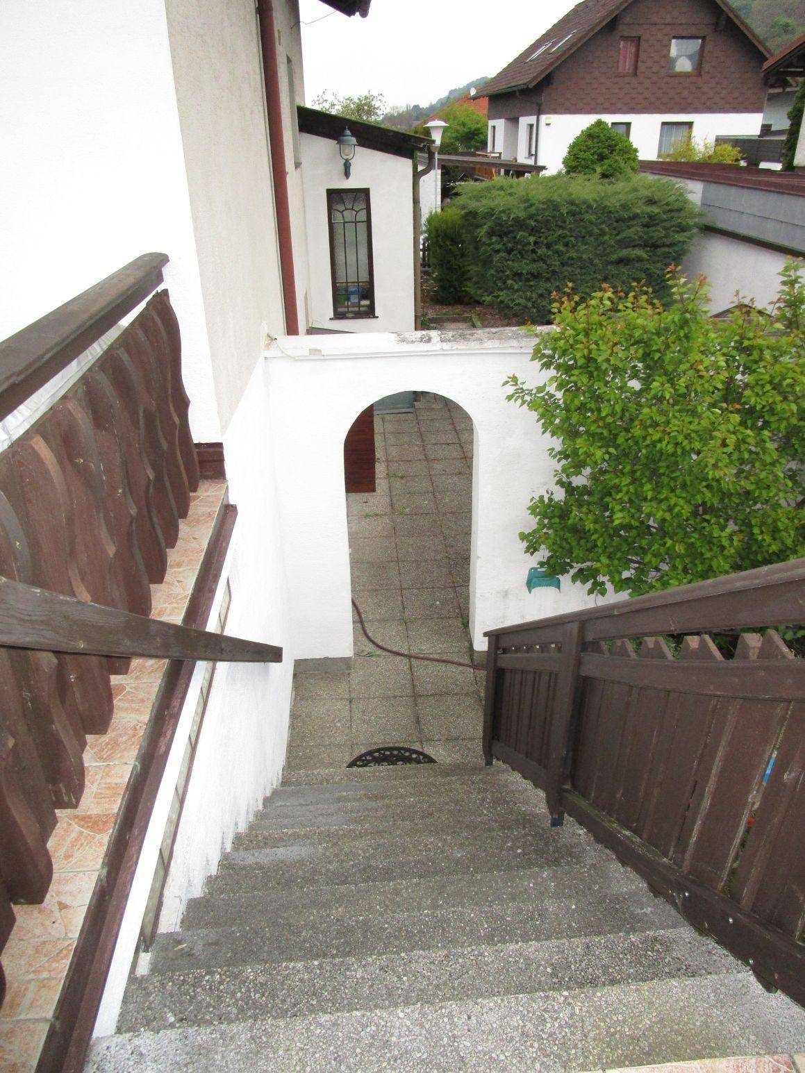 Außentreppe führt hinunter zu einem gewölbten Eingangsbereich des Hauses.