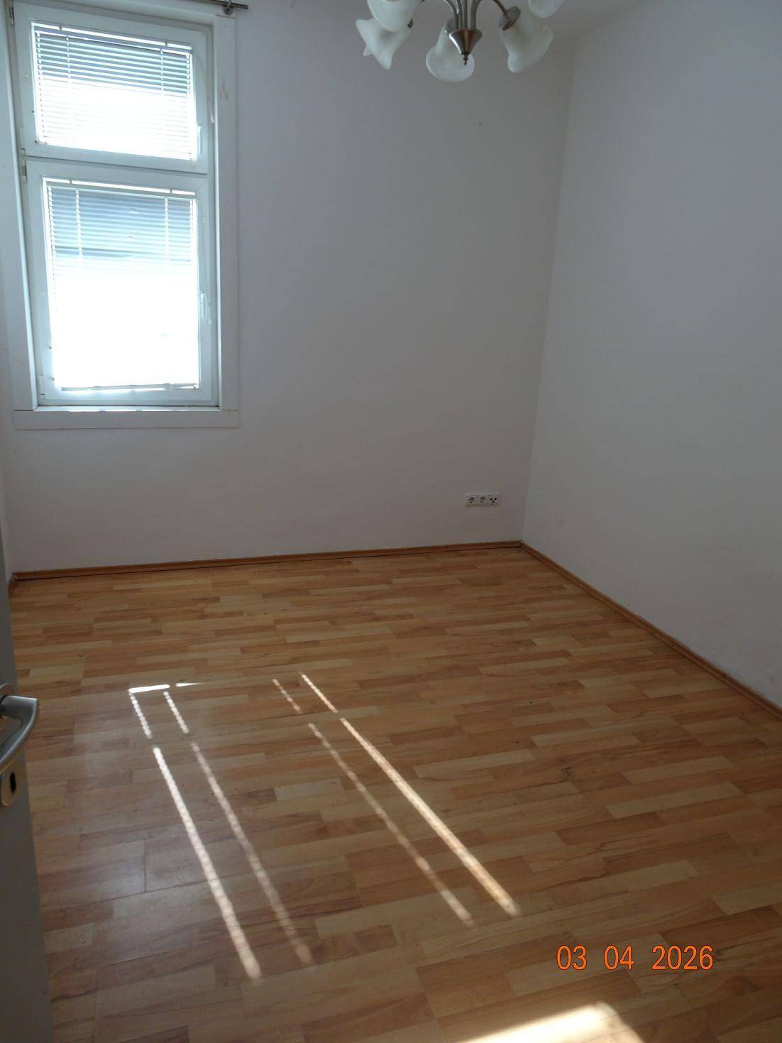 Heller Raum mit Laminatboden und einem Fenster, das Sonnenlicht auf den Boden wirft.