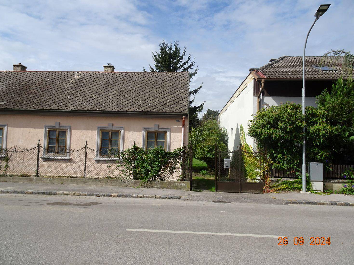 Straßenansicht eines Hauses mit rosa Fassade und dem Eingangstor zum Grundstück.