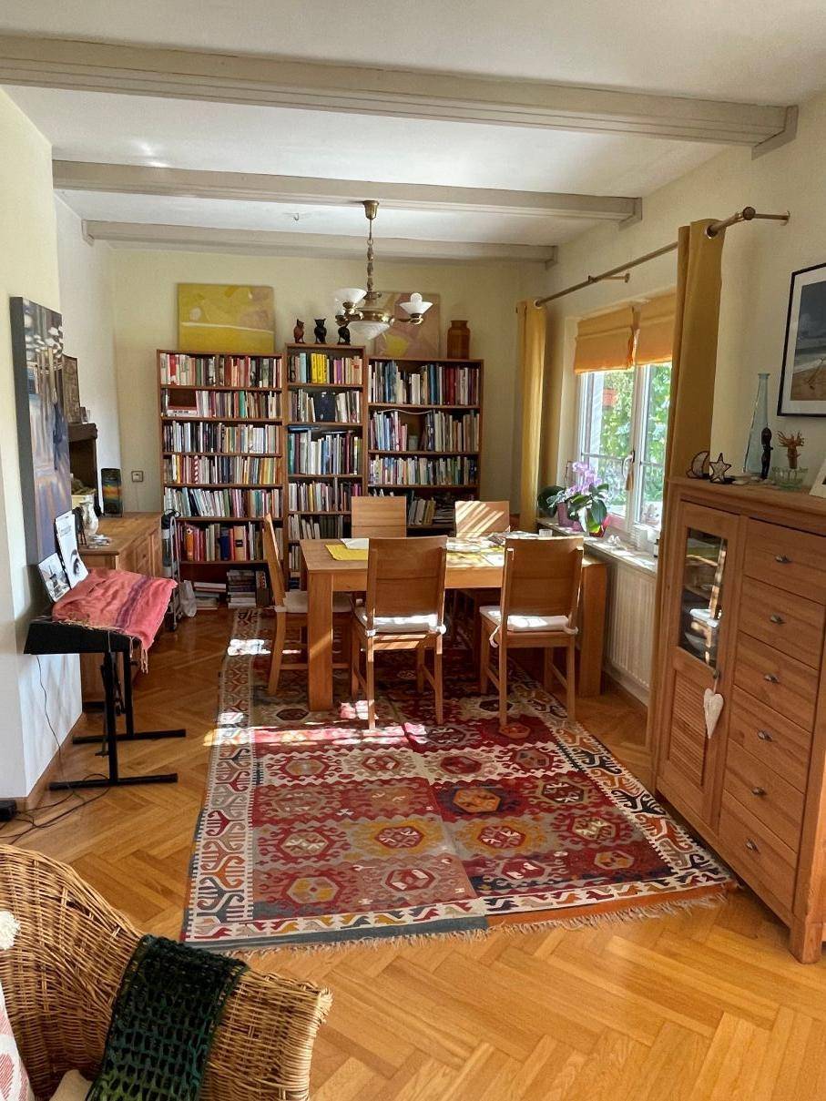 Essbereich mit Holztisch, Bücherregalen und Fischgrätparkett in einem offenen Wohnraum.