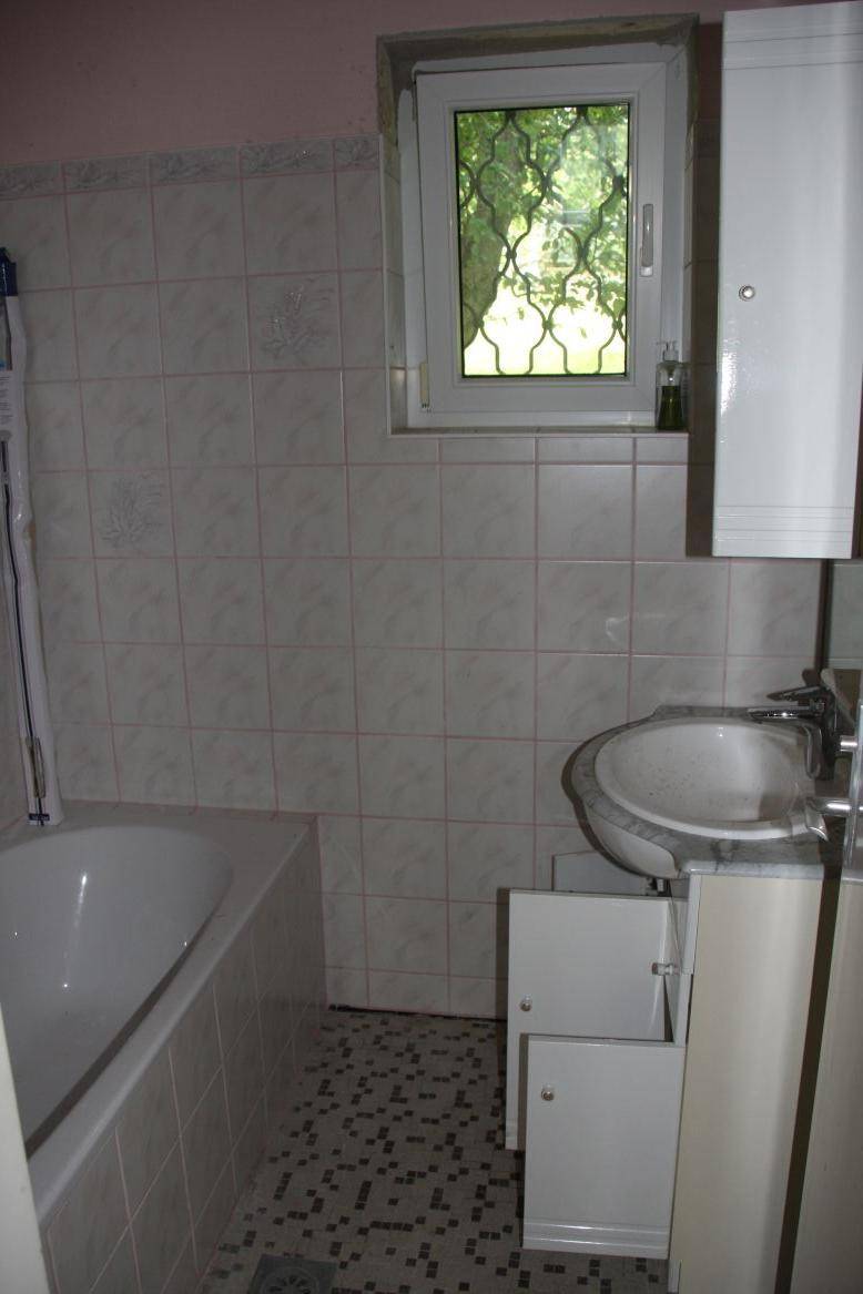Badezimmer mit Badewanne, Waschbecken und Fenster, zeigt ältere Fliesen und Ausstattung.