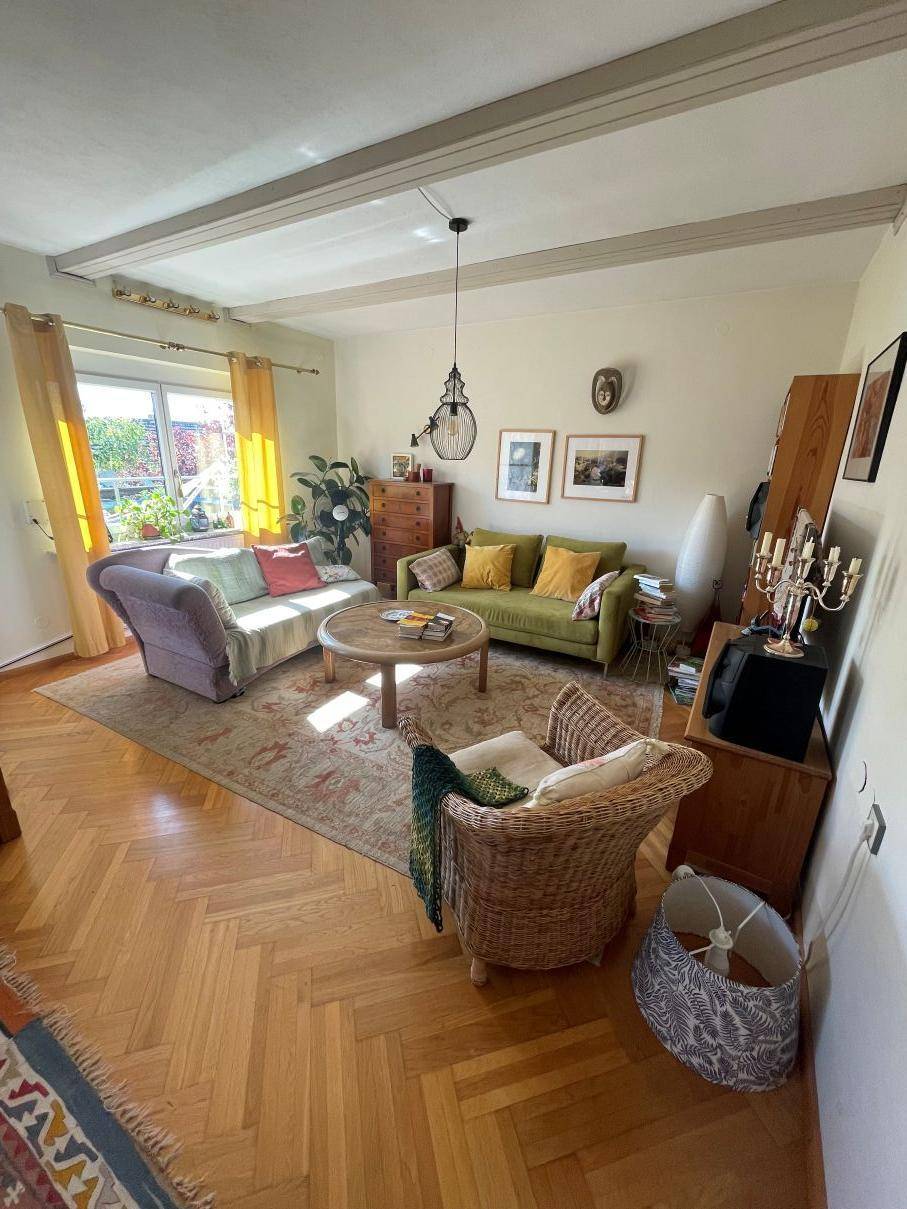 Helles Wohnzimmer mit Fischgrätparkett, gemütlichen Sofas und sichtbaren Deckenbalken.
