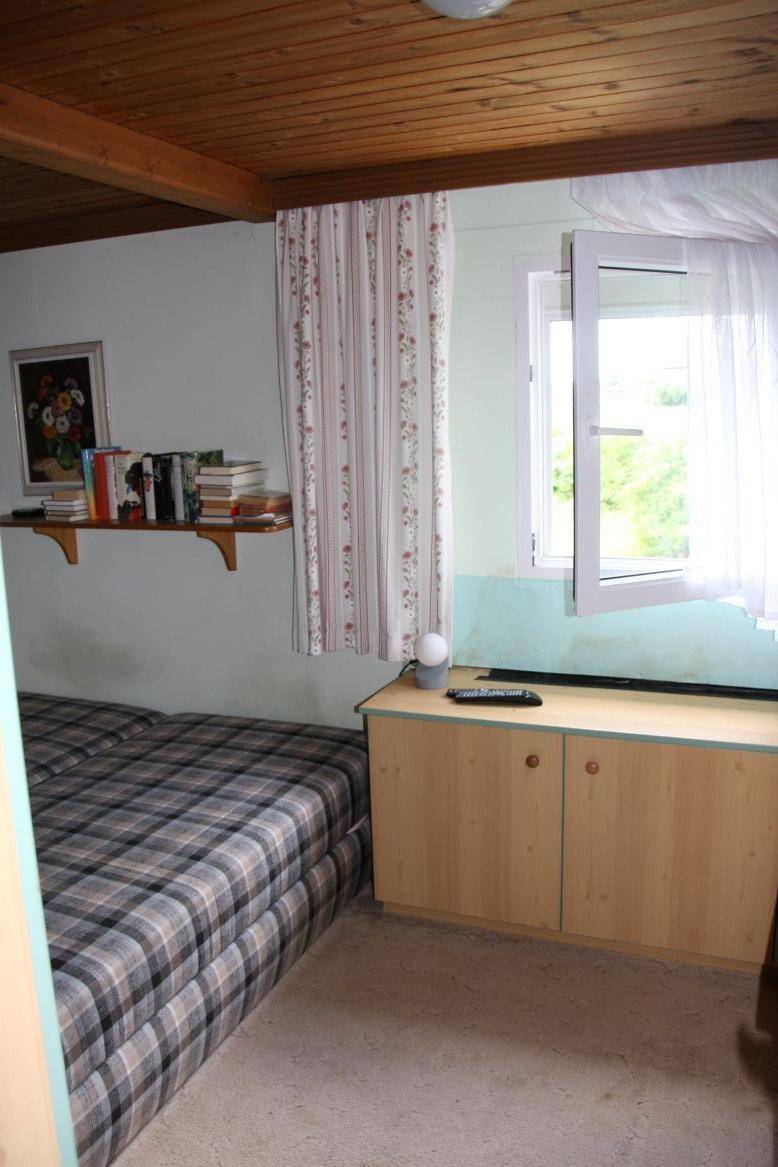 Schlafzimmer mit kariertem Bett, Holzdecke und Fenster mit Blick ins Grüne.