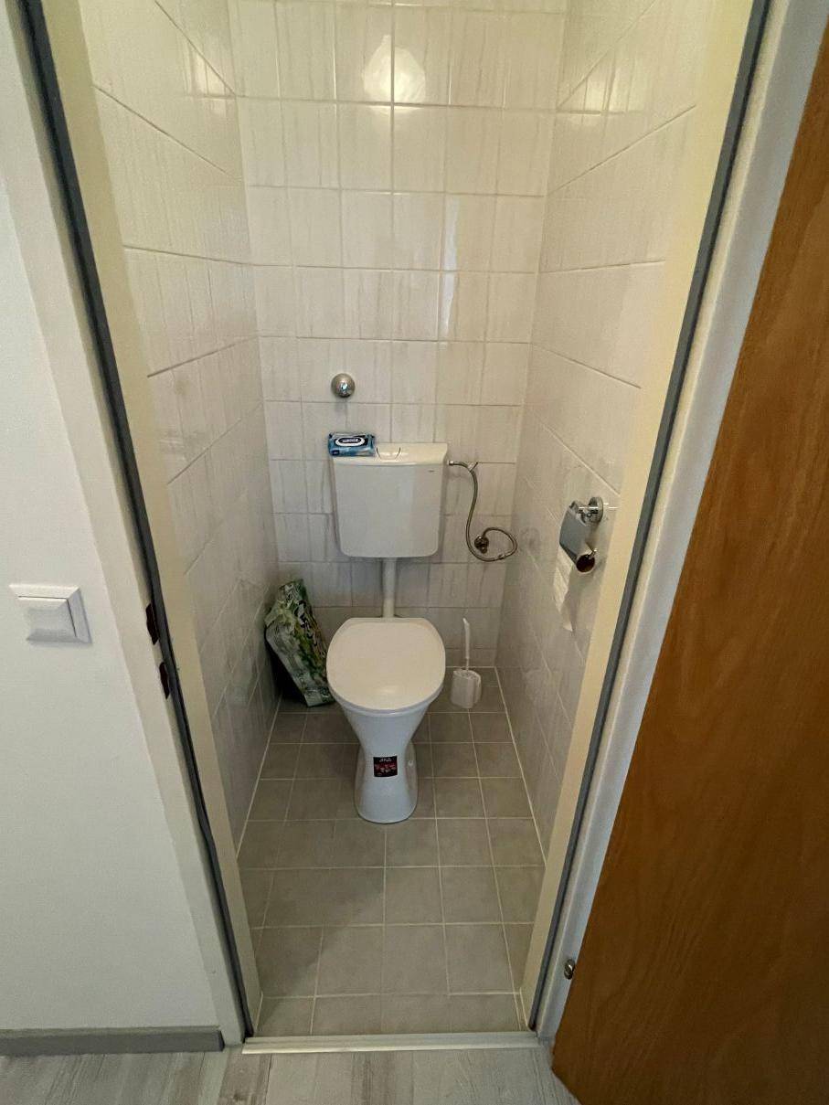 Separates WC mit Fliesenboden und Wänden, ausgestattet mit einer Toilette.