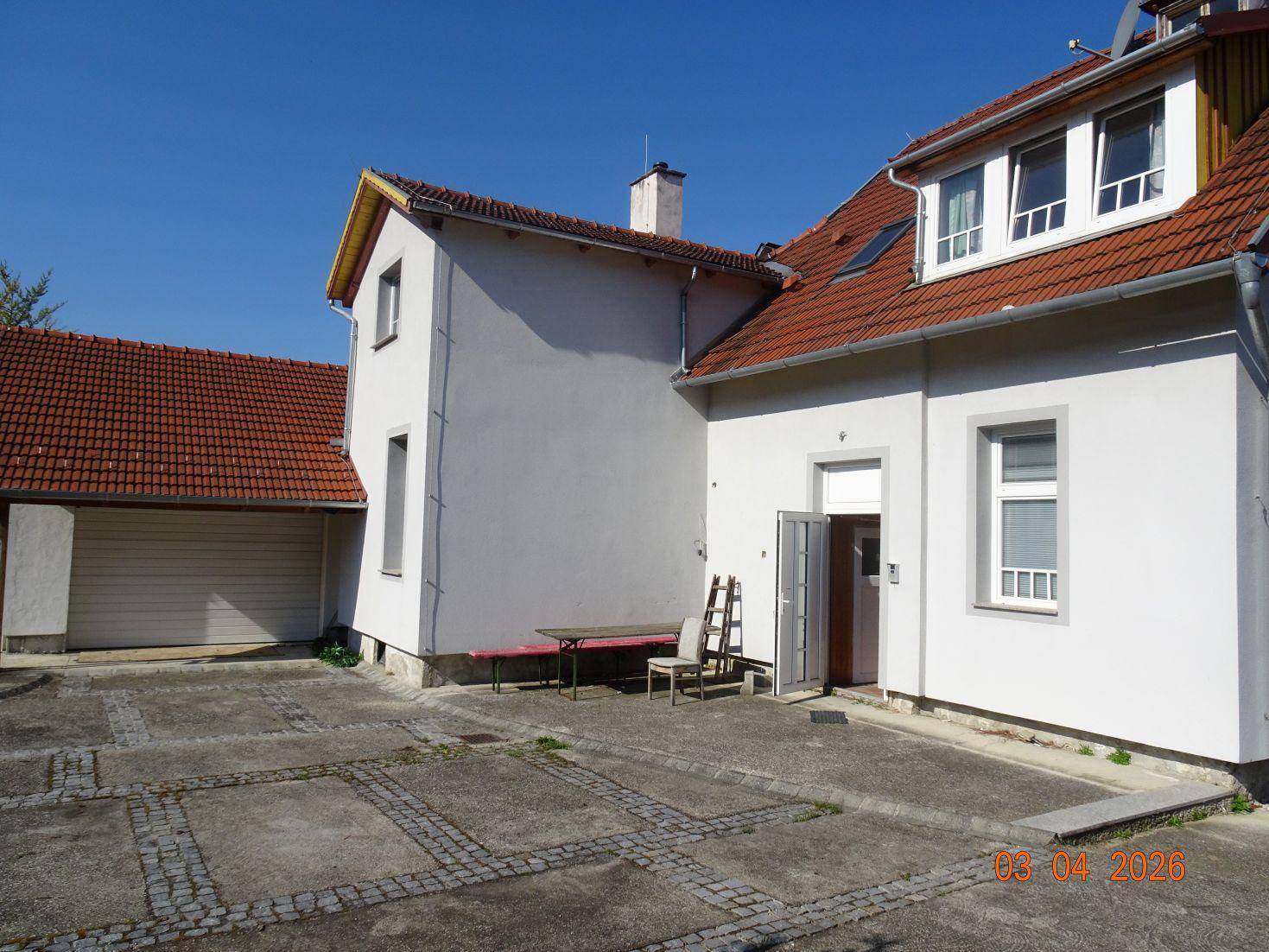 Gepflasterter Hinterhof mit Garage und der Rückseite des Wohnhauses unter blauem Himmel.