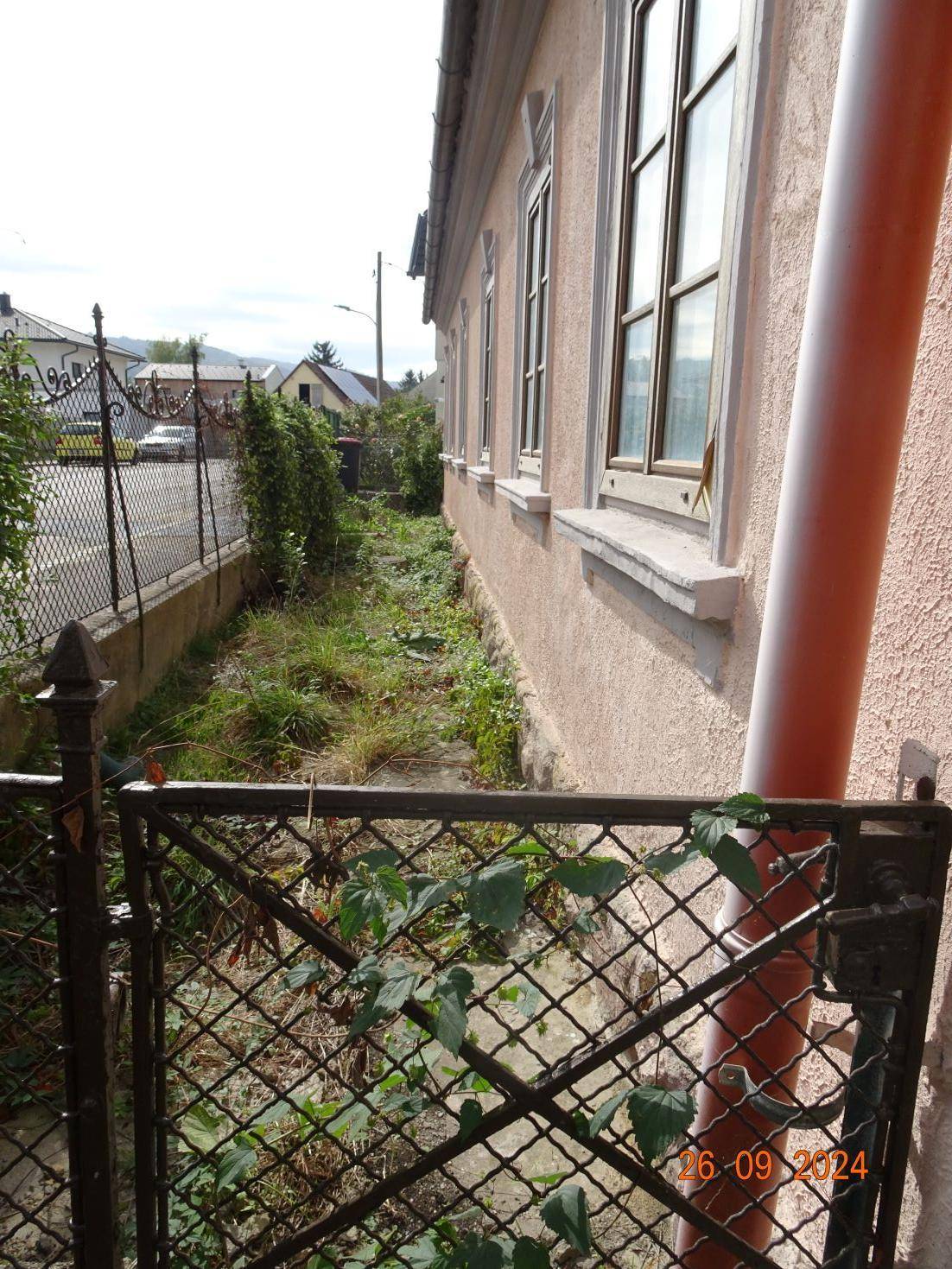 Seitenansicht des Hauses mit einem schmalen Weg entlang der Fassade und einem Zaun.