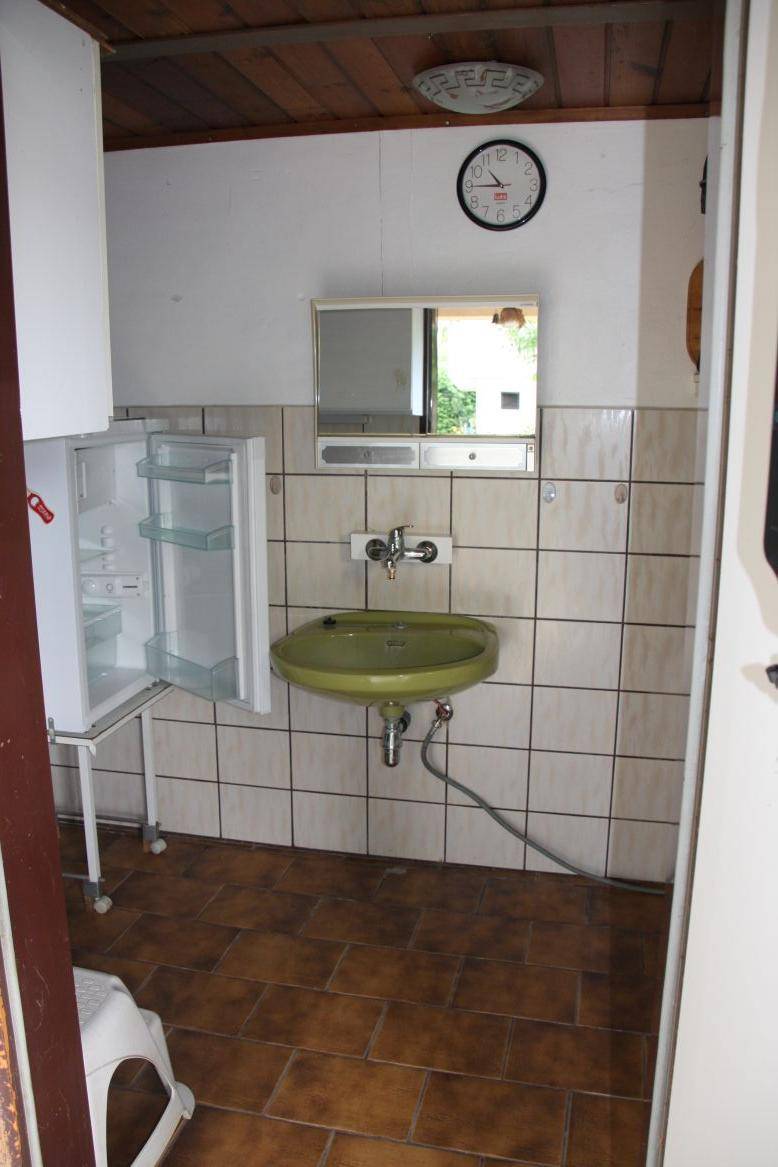 Einfacher Waschraum mit grünem Waschbecken, Fliesen und kleinem Kühlschrank.