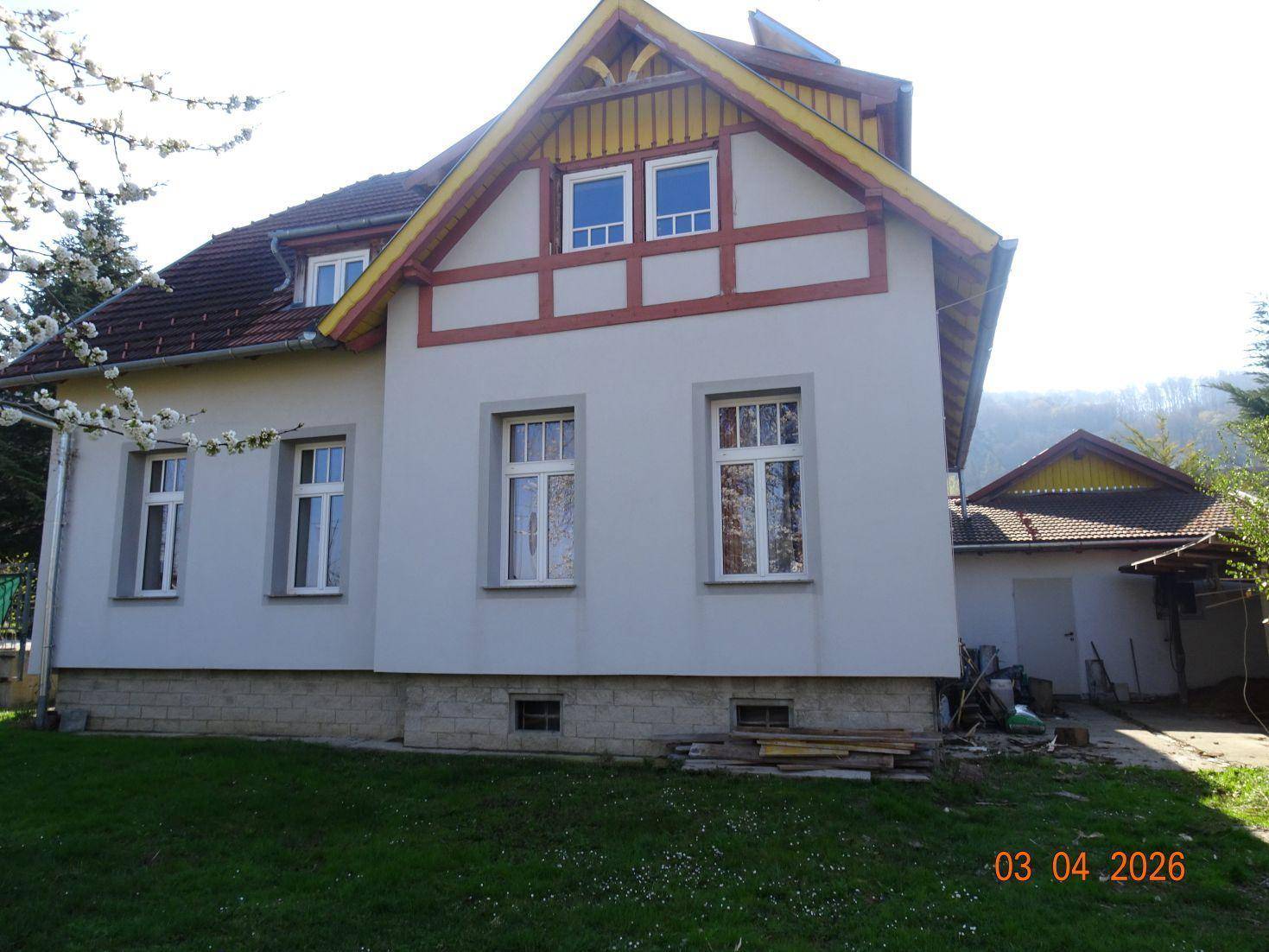 Seitenansicht des Hauses mit traditionellen Holzelementen und einem Anbau unter blauem Himmel.