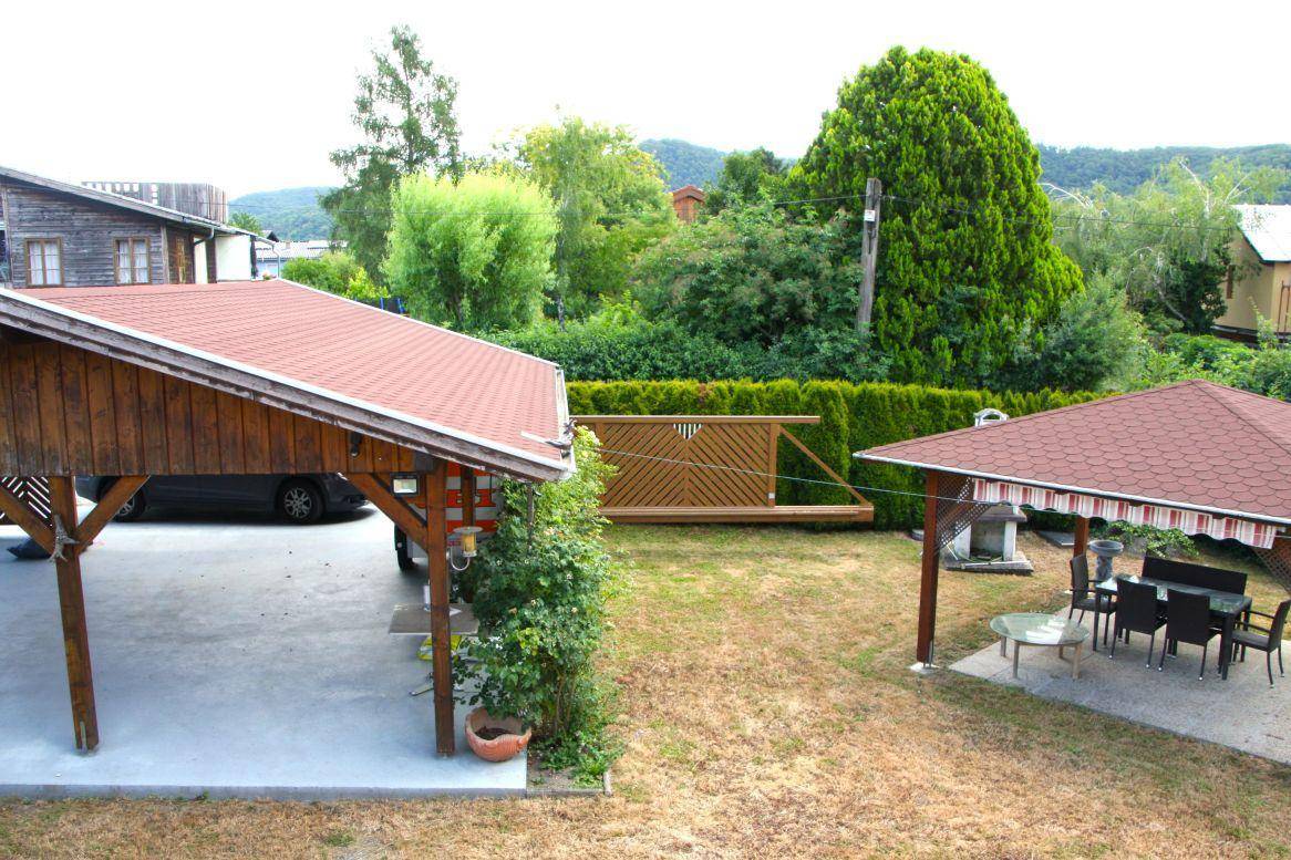 Großer Gartenbereich mit Carport, hoher Hecke und überdachtem Essbereich im Freien.
