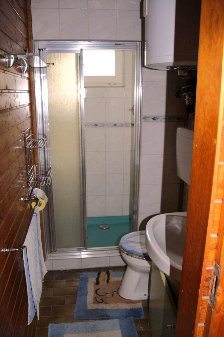 Kleines Badezimmer mit Duschkabine, WC und Holzverkleidung an den Wänden.