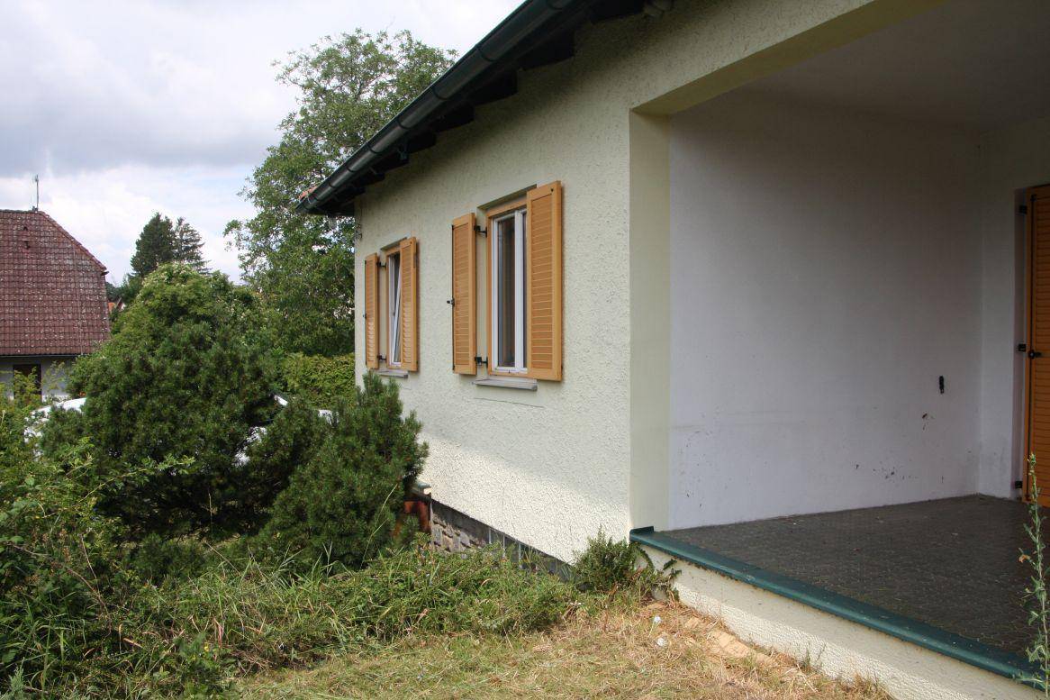 Seitenansicht des Hauses mit hellen Fensterläden und einem überdachten Eingangsbereich.