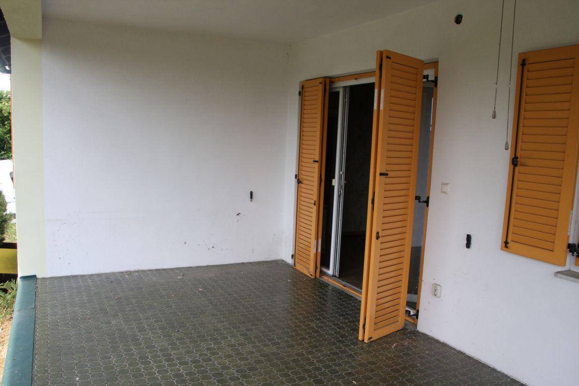 Überdachter Außenbereich mit Fliesenboden und geöffneten Fensterläden, bietet Zugang zum Innenraum.