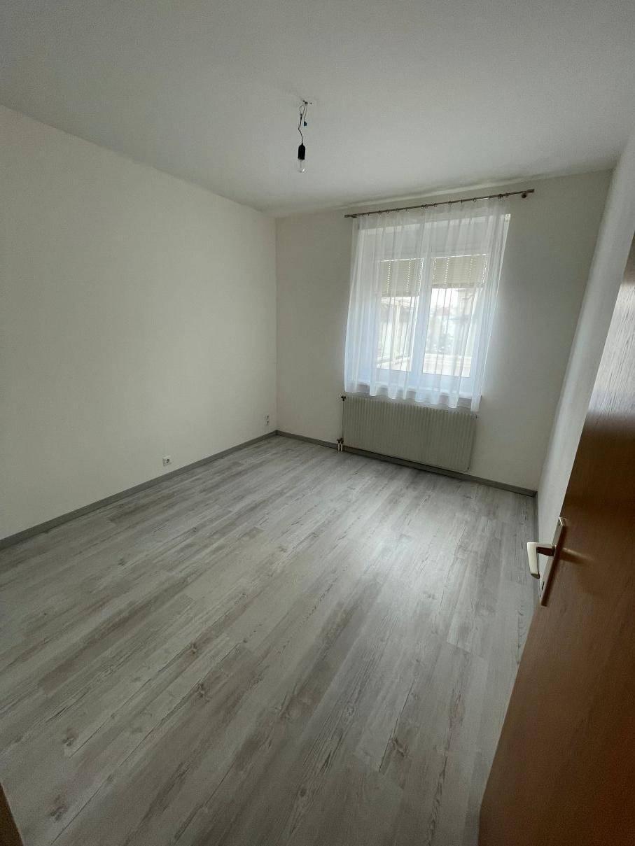 Leeres Schlafzimmer mit hellem Laminatboden, weißen Wänden und einem Fenster.