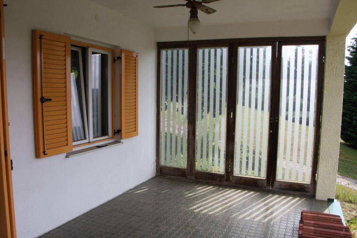 Überdachte Loggia mit gemusterten Glastüren und einem Fenster mit geöffneten Fensterläden.