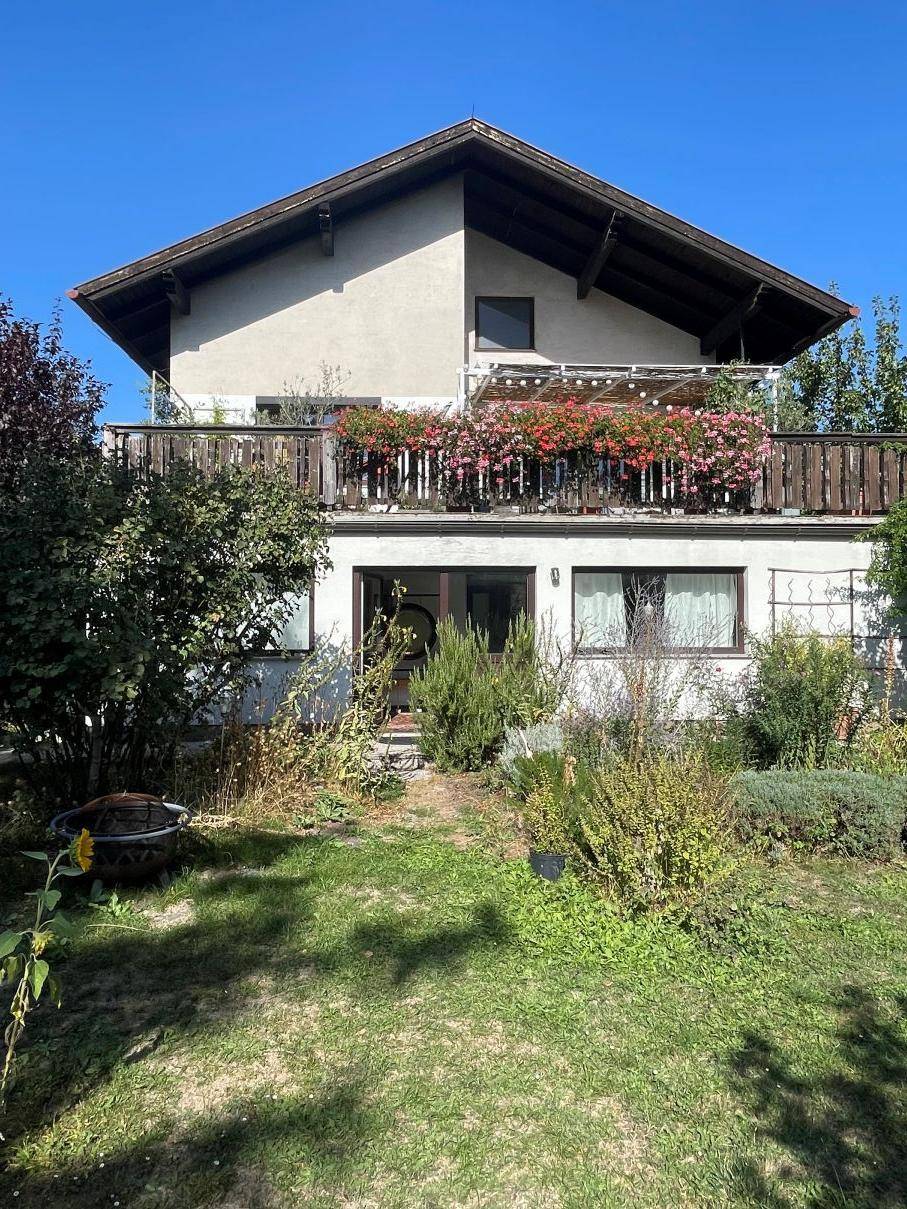 Rückansicht des Hauses mit Balkon und blühenden Blumenkästen sowie Gartenbereich.