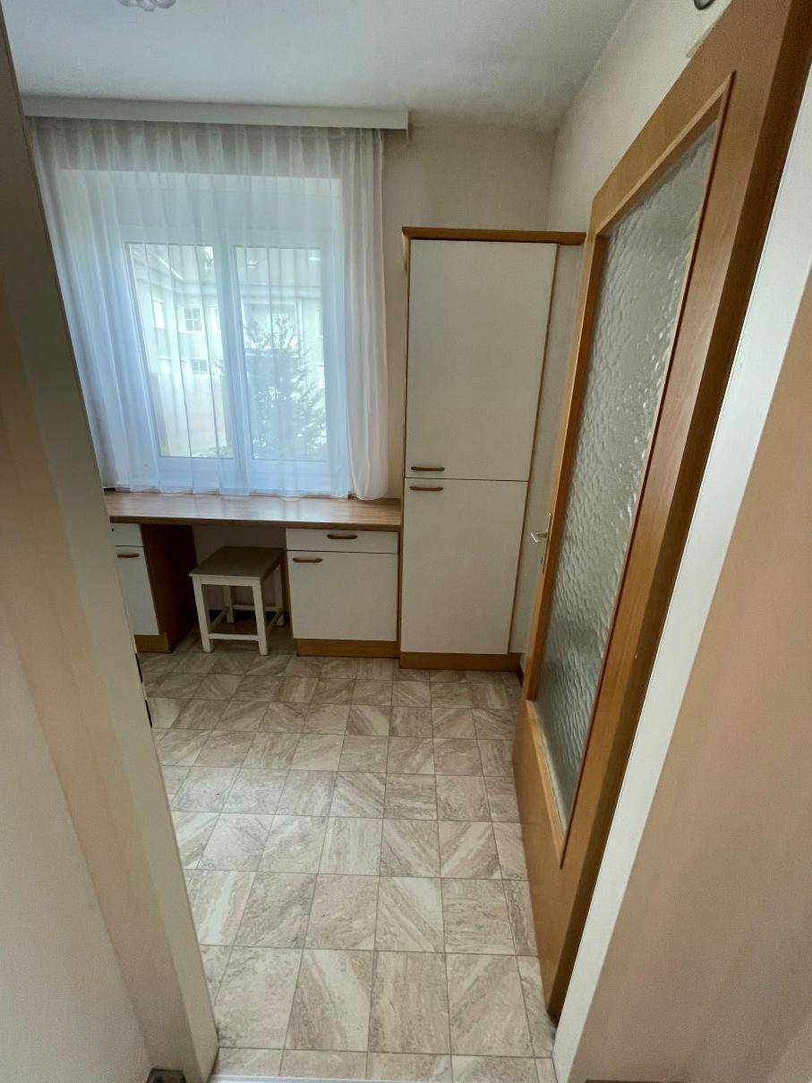 Kleines Arbeitszimmer mit Fliesenboden, Fenster und praktischen Einbauschränken.