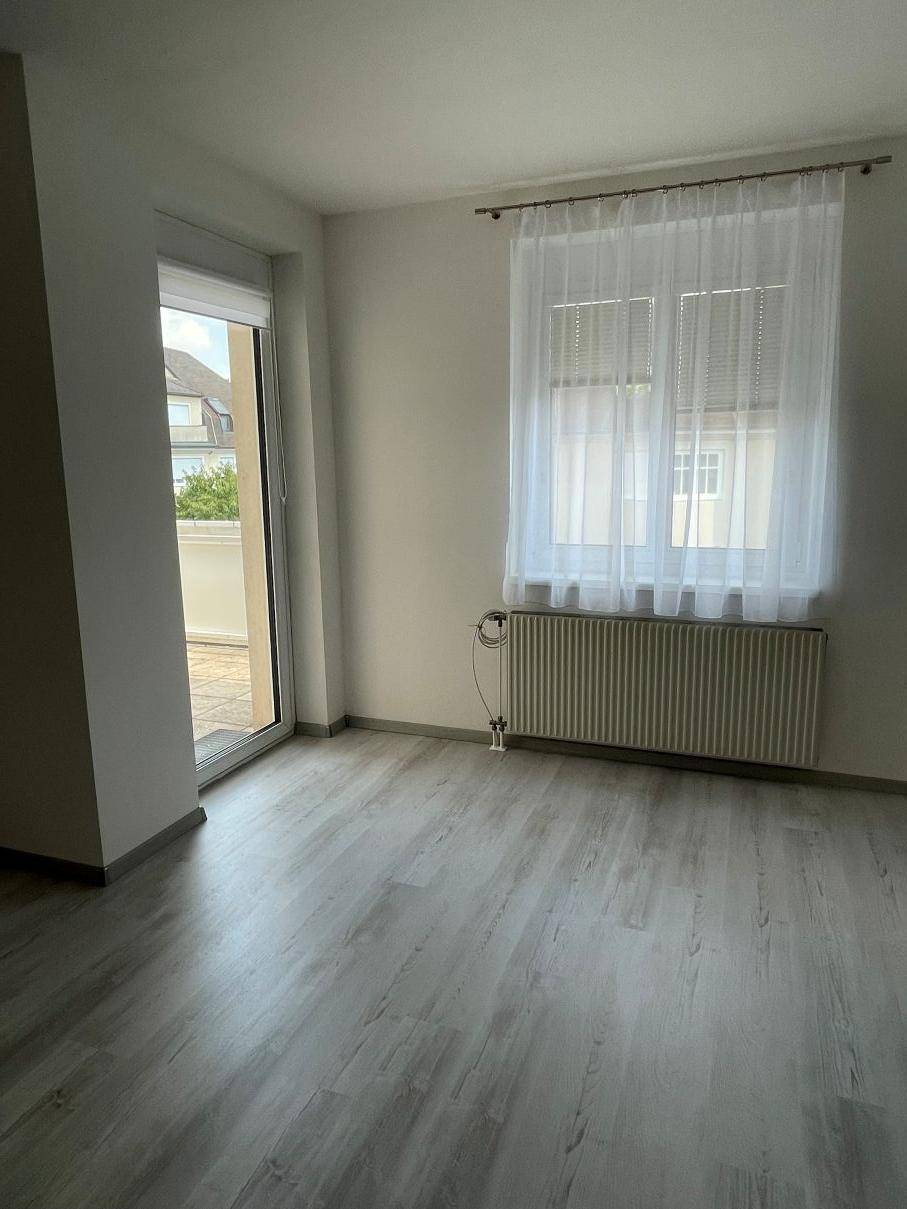 Raum mit hellem Laminatboden, Fenster und Zugang zu einem Außenbereich.