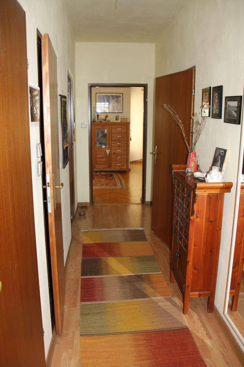 Heller Flur mit Holztüren, farbenfrohem Teppich und einem Holzschrank.