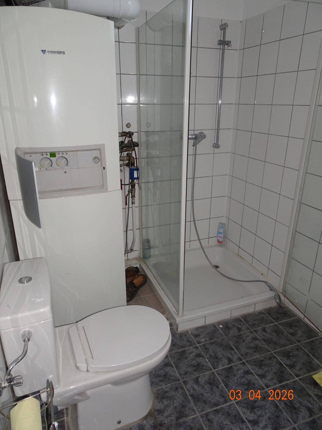 Badezimmer mit Toilette, Duschkabine und Heizungsanlage an der Wand.