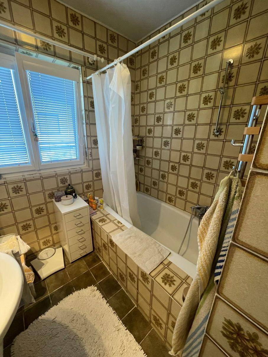 Badezimmer mit gemusterten Fliesen, Badewanne mit Duschvorhang und Fenster.