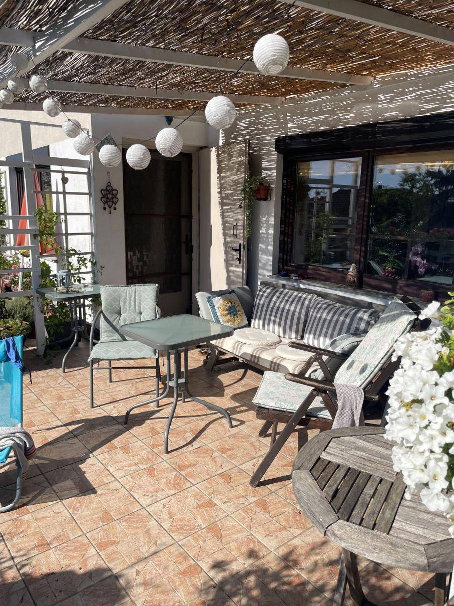 Sonnige Terrasse mit Fliesenboden, Gartenmöbeln und einer Pergola als Sonnenschutz.