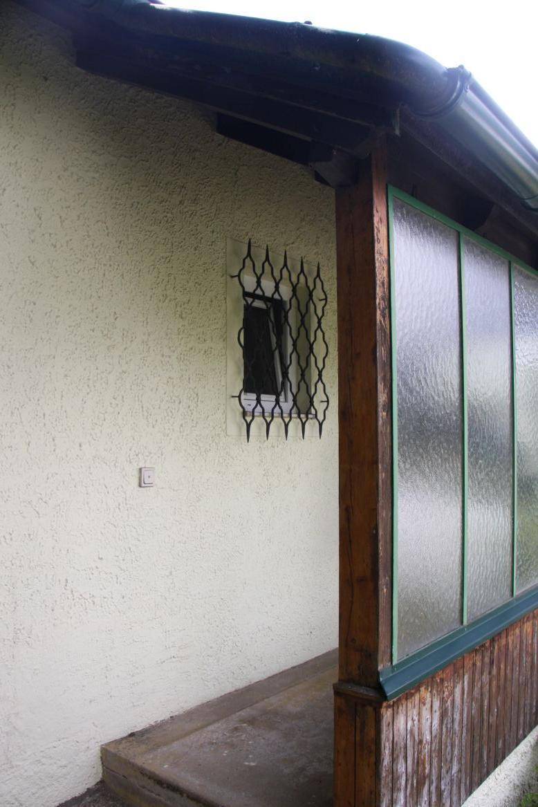 Fenster mit schmiedeeisernem Gitter und angrenzendem verglastem Anbau, möglicherweise ein Wintergarten.
