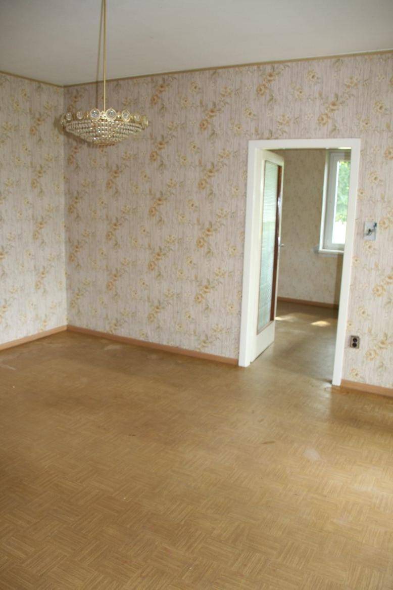 Leeres Zimmer mit gemusterter Tapete und einem Kronleuchter, bereit für die Renovierung.