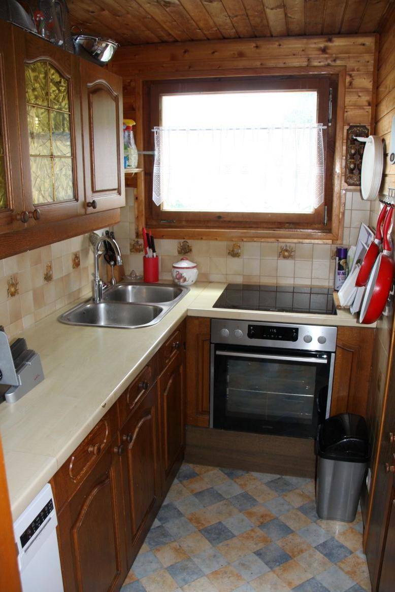 Kleine Küche mit Holzschränken, Fliesenboden und Fenster über der Spüle.