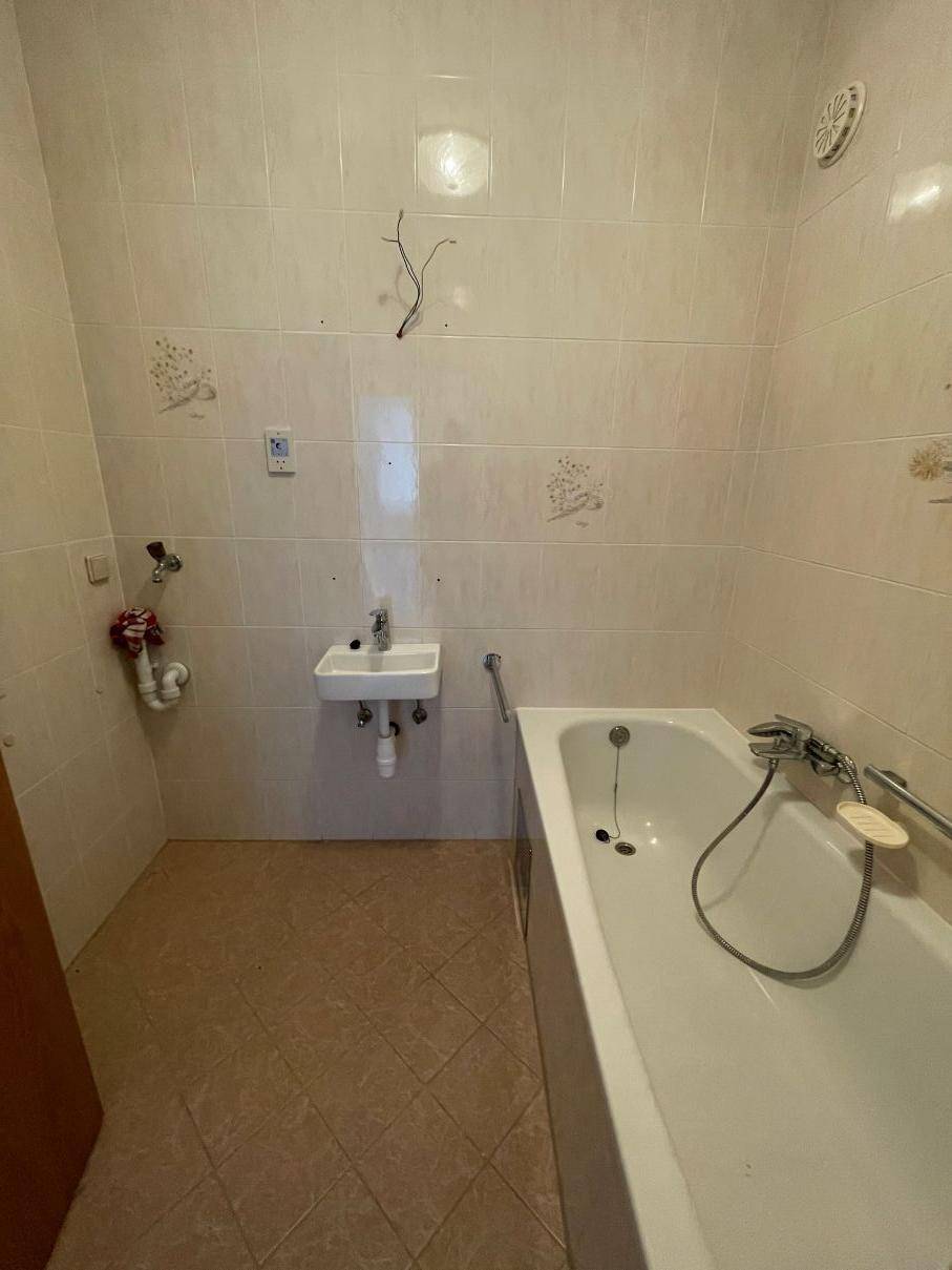 Badezimmer mit Badewanne, kleinem Waschbecken und gefliesten Wänden und Boden.