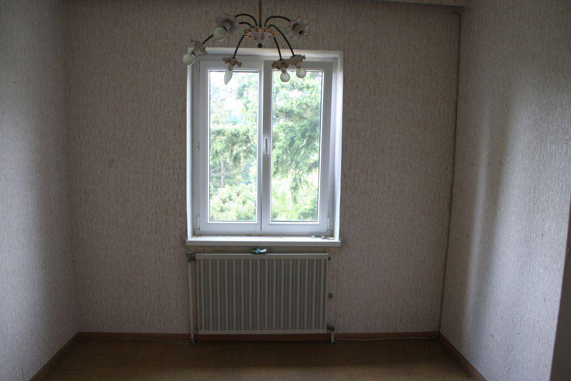 Leeres Zimmer mit Fenster, Heizkörper und einfacher Deckenleuchte, wartet auf neue Gestaltung.