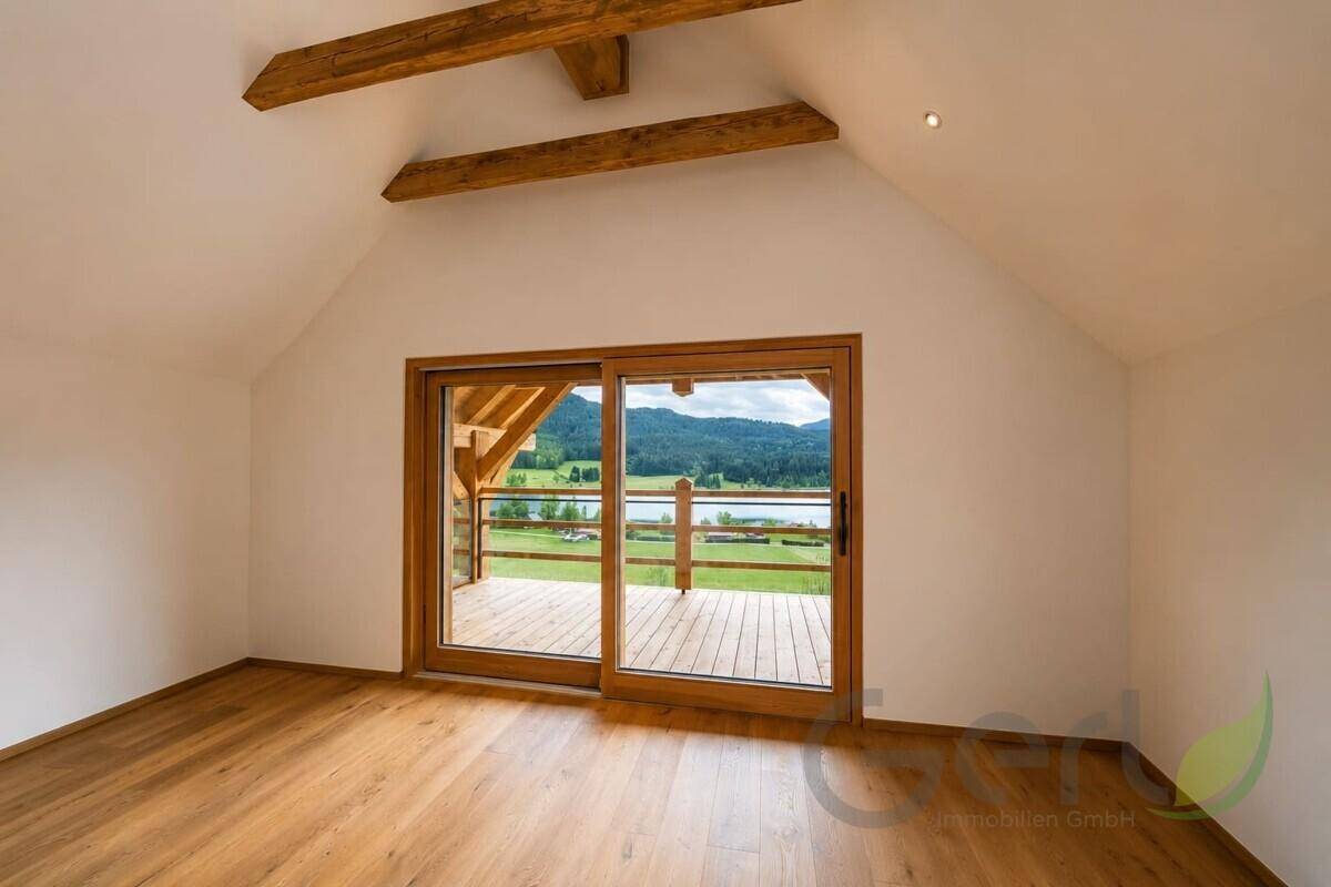 Helles Zimmer mit Holzboden, Dachschräge und Zugang zu einem Balkon mit Seeblick.