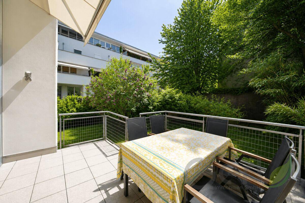 Geflieste Terrasse mit Esstisch und Stühlen, umgeben von grünen Pflanzen und Bäumen.