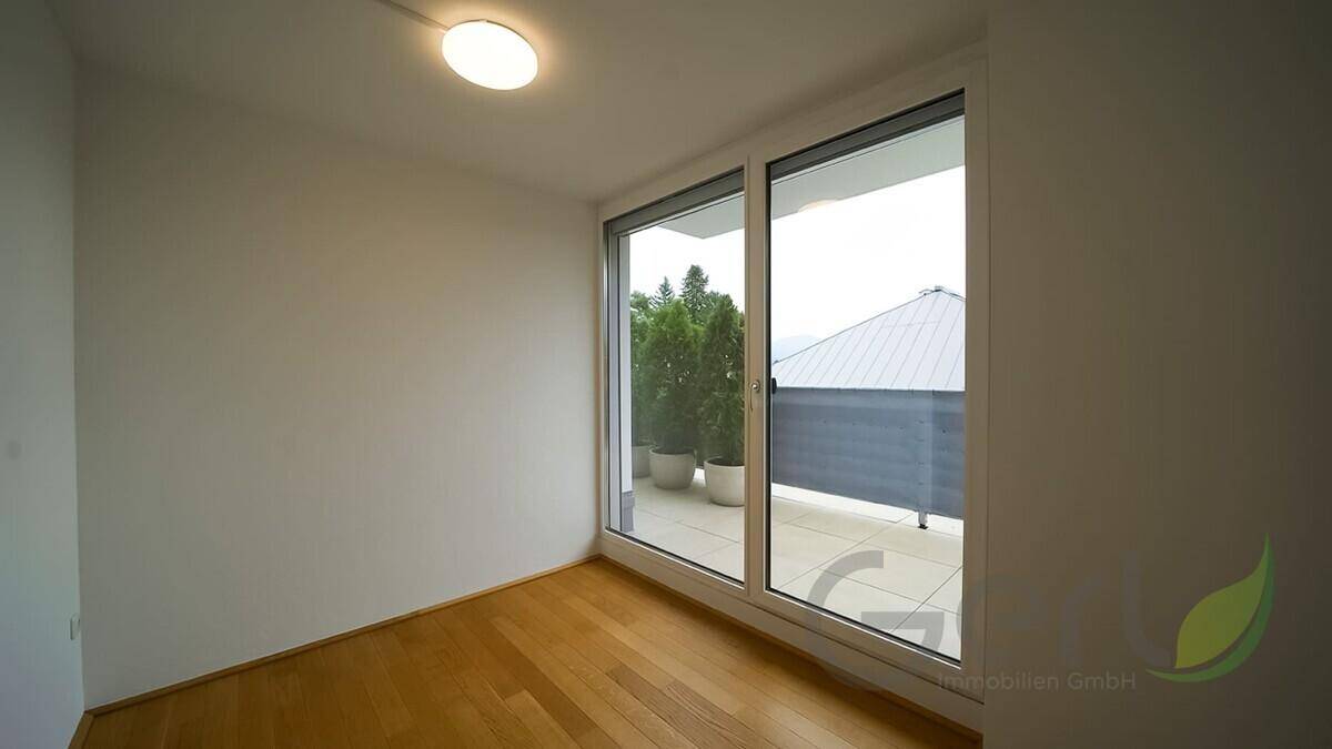 Lichtdurchflutetes Zimmer mit hellem Holzfußboden und großen Fenstern, die den Blick nach draußen öffnen.