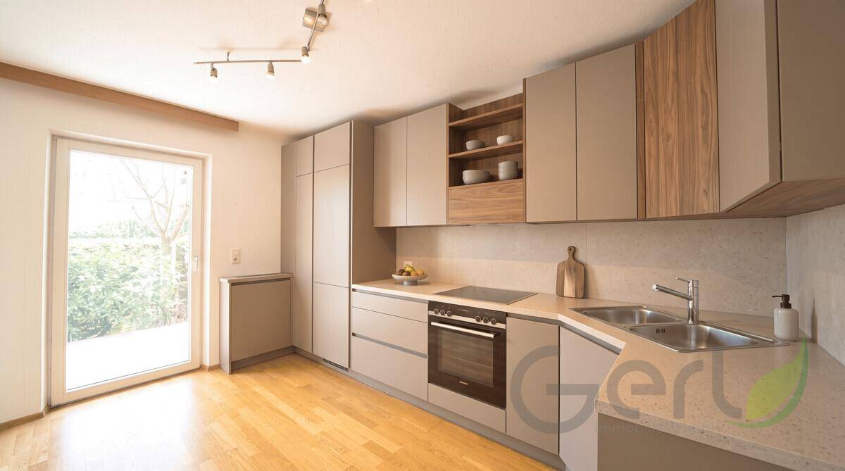Moderne Einbauküche mit hellgrauen Fronten, Holzakzenten und Zugang zum Außenbereich.