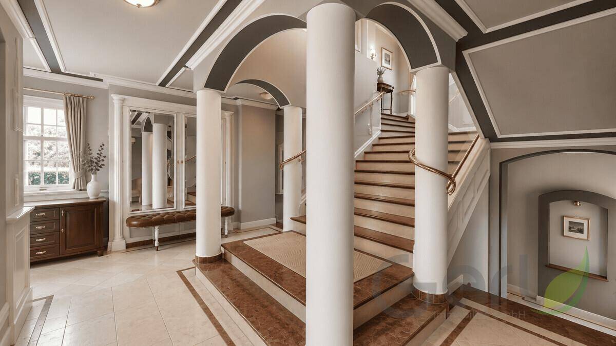 Heller Flur mit eleganter Treppe, Säulen und Marmorboden, der zu den oberen Etagen führt.