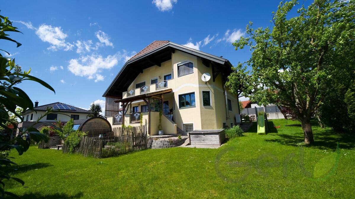 Rückseite des Hauses mit großem Rasen, Bäumen und einem Spielbereich mit Rutsche für Kinder.