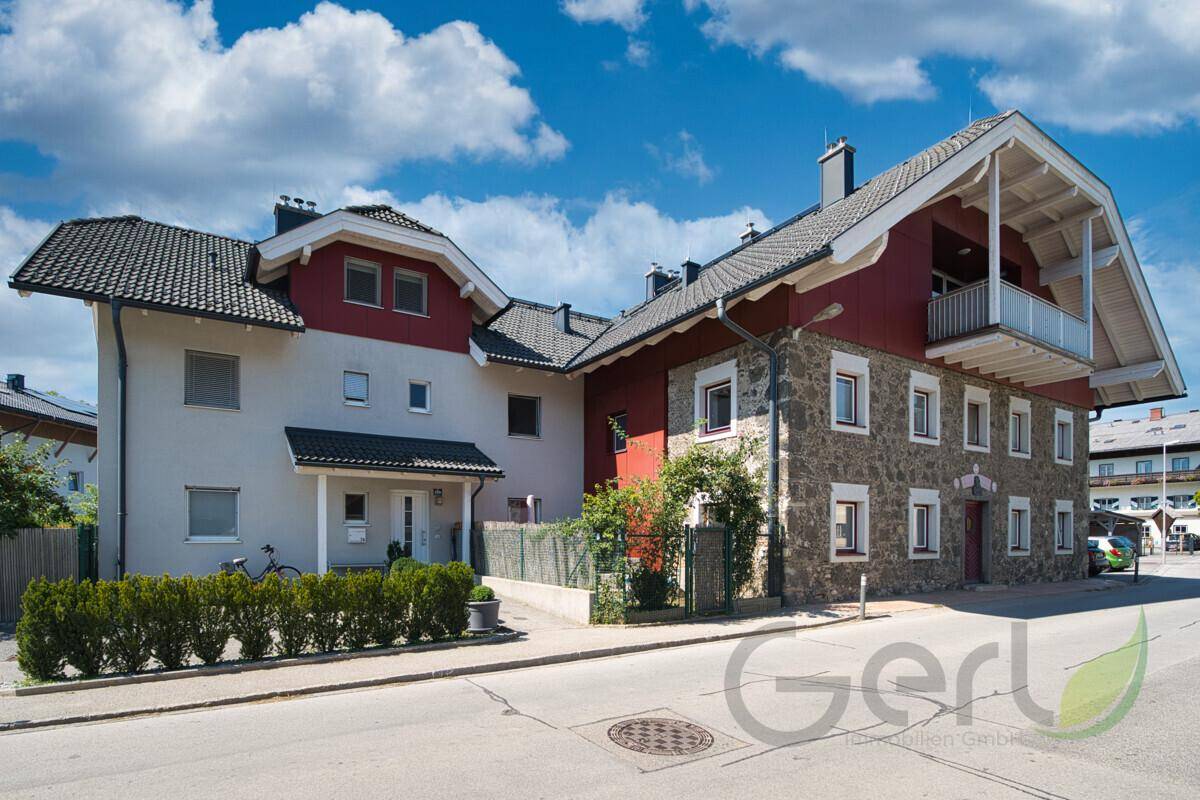 Seitenansicht des Gebäudes mit moderner Architektur, Steinfassade und gepflegter Hecke.