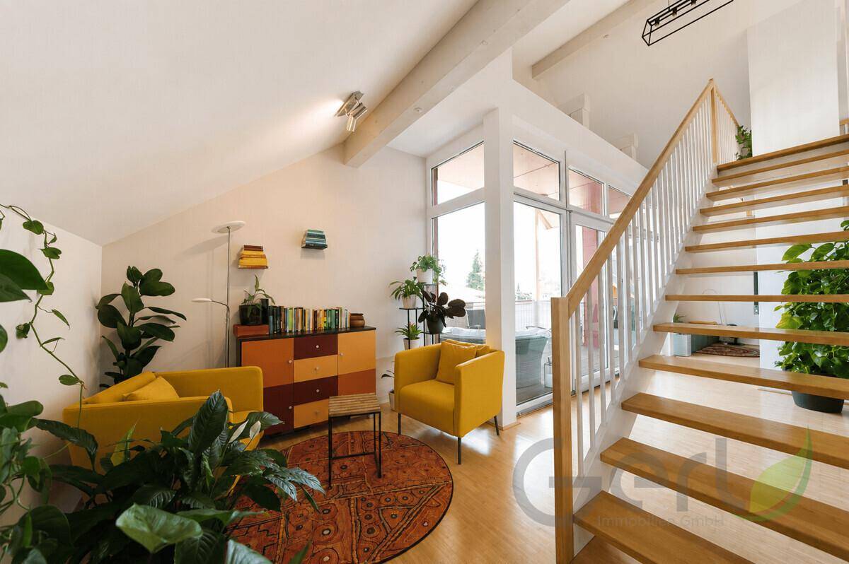 Heller Wohnbereich mit gelben Sesseln, Bücherregal und Zugang zum Balkon über große Fenster.