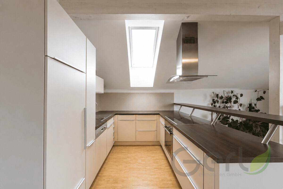 Moderne Küche mit weißen Schränken, dunklen Arbeitsplatten und einem Dachfenster für viel Licht.