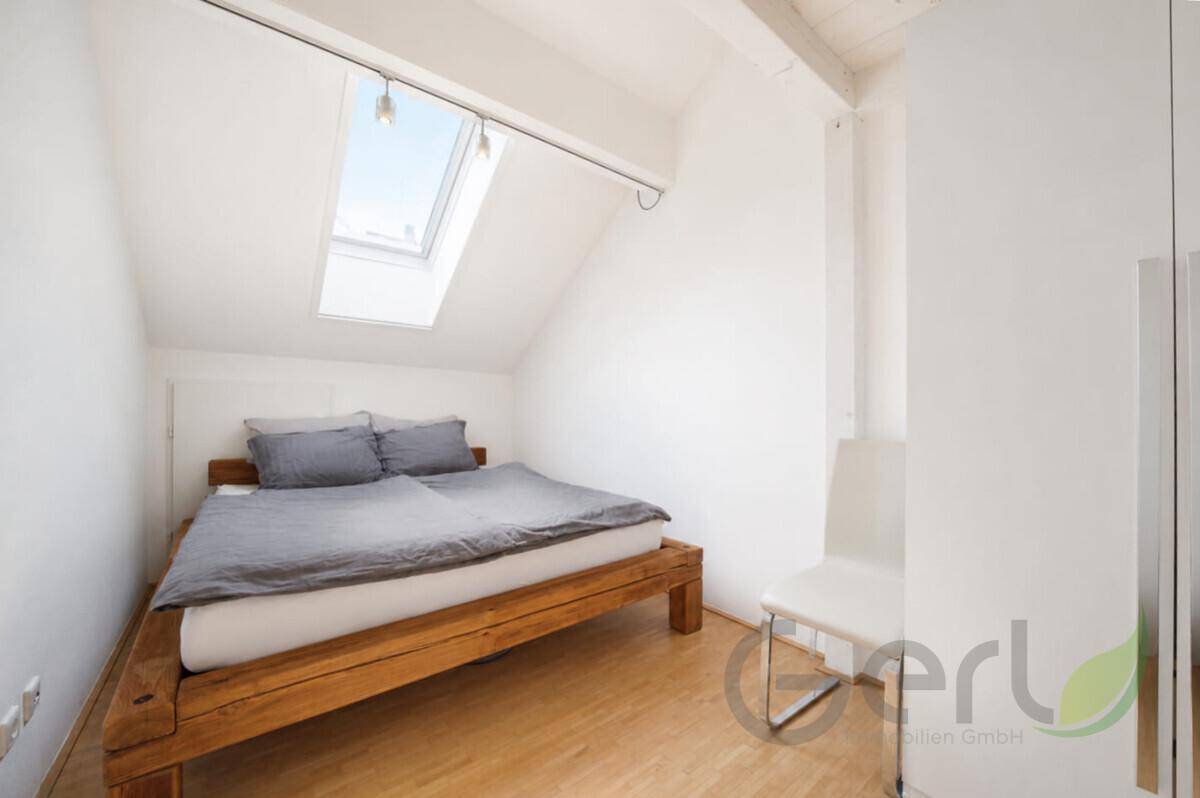 Gemütliches Schlafzimmer im Dachgeschoss mit Holzbett, Dachfenster und schrägen Wänden.