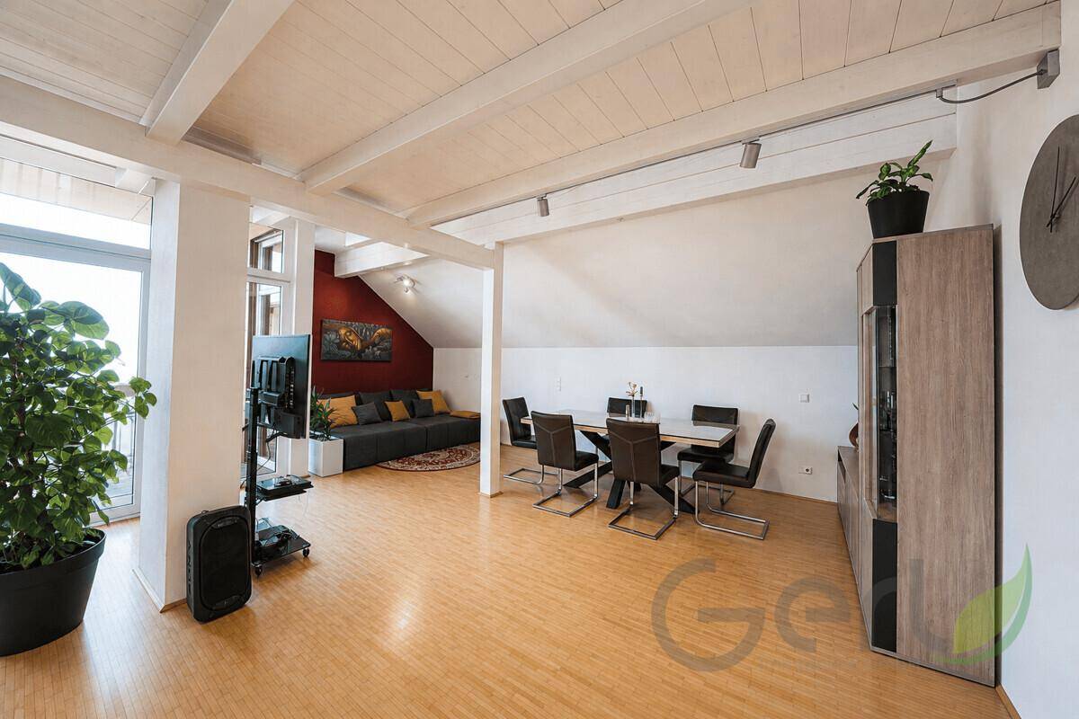 Offener Wohn- und Essbereich mit Holzboden, roter Akzentwand und viel Tageslicht.