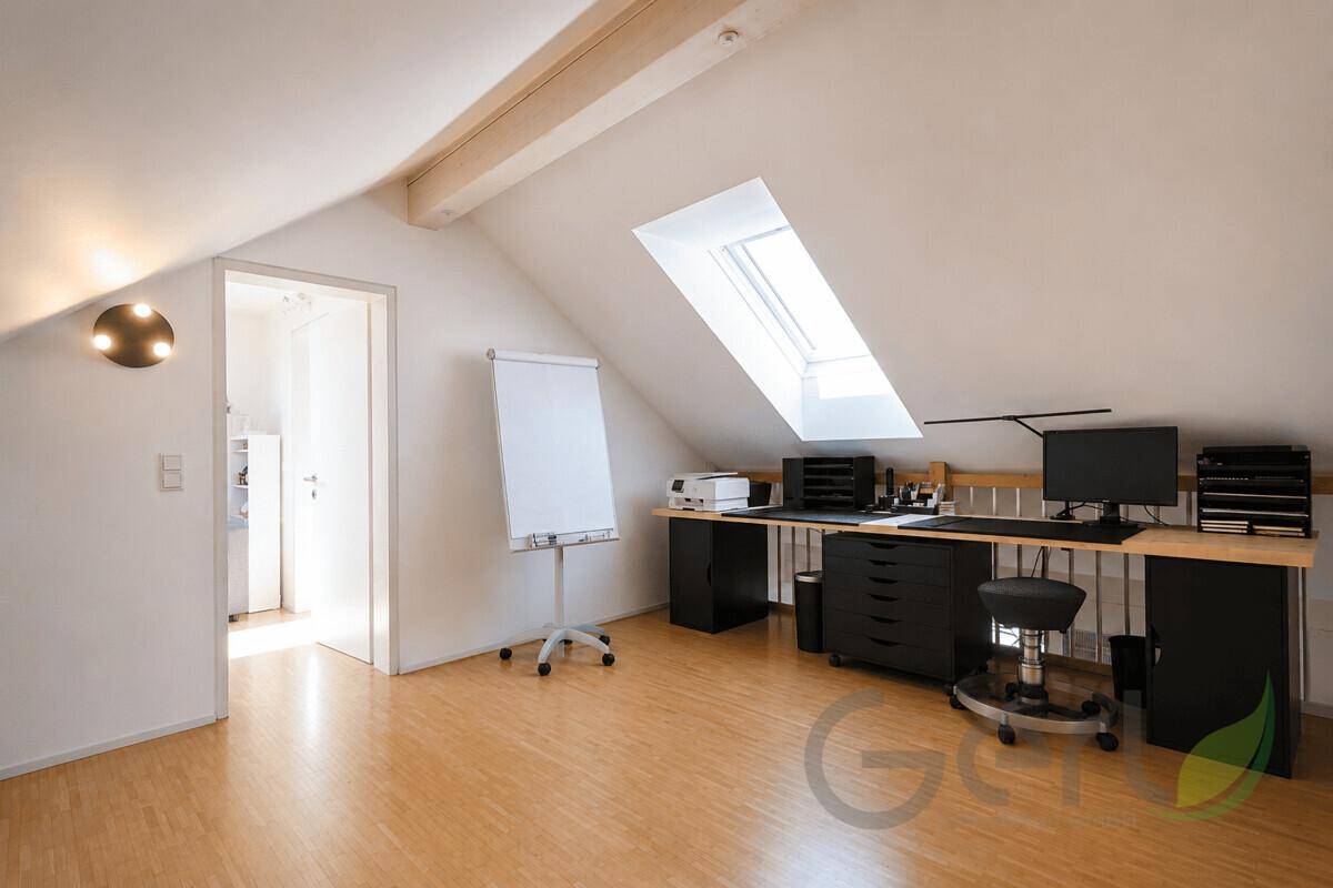 Helles Arbeitszimmer im Dachgeschoss mit Schreibtisch, Computer und einem großen Dachfenster.