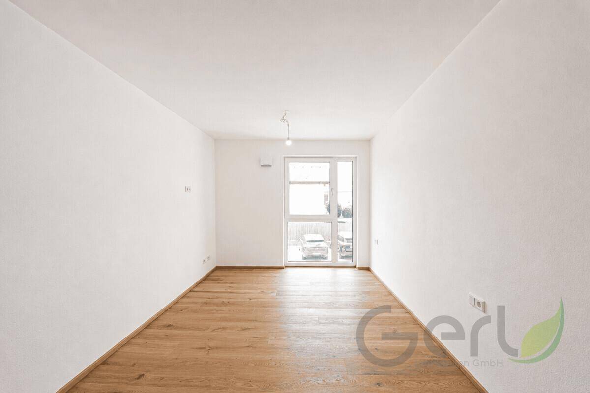 Helles, leeres Zimmer mit Holzboden und großer Fenstertür, ideal als Schlaf- oder Gästezimmer.