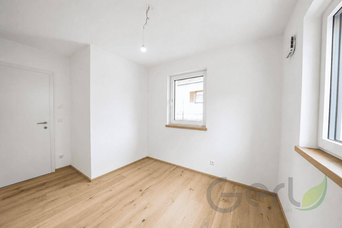 Leeres, helles Zimmer mit Holzboden und Fenster, geeignet als Büro oder Gästezimmer.