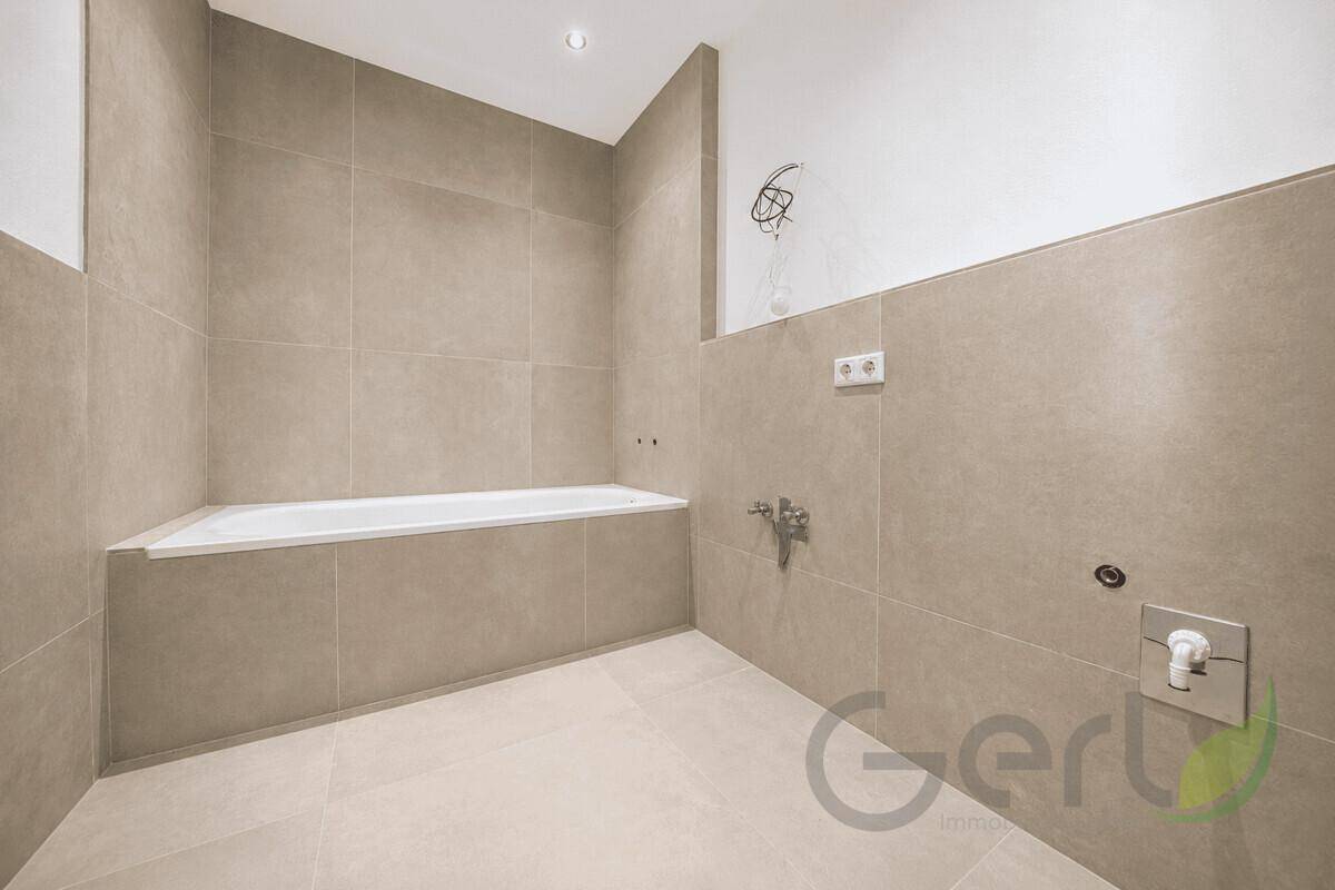 Unmöbliertes Badezimmer mit Badewanne und beigefarbenen Fliesen, bereit für die Einrichtung.
