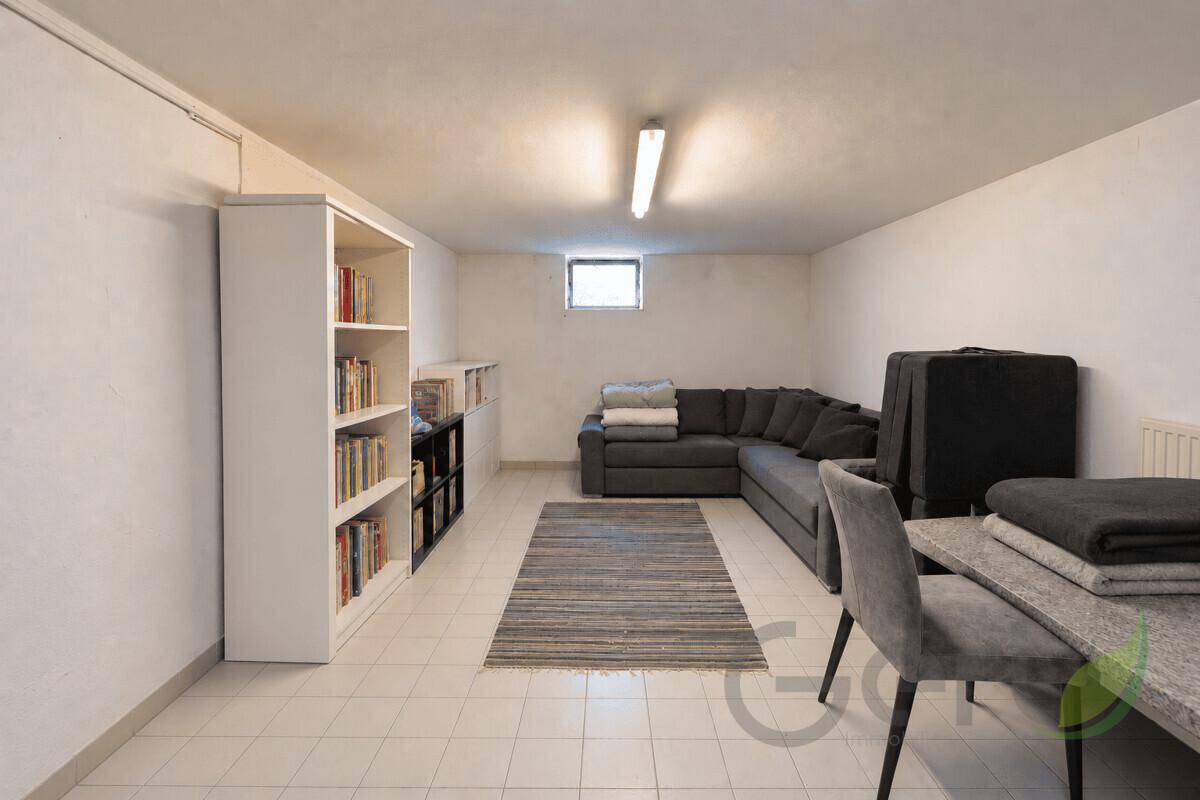 Ausgebauter Kellerraum mit Sofa, Bücherregalen und Fliesenboden, nutzbar als Hobbyraum.