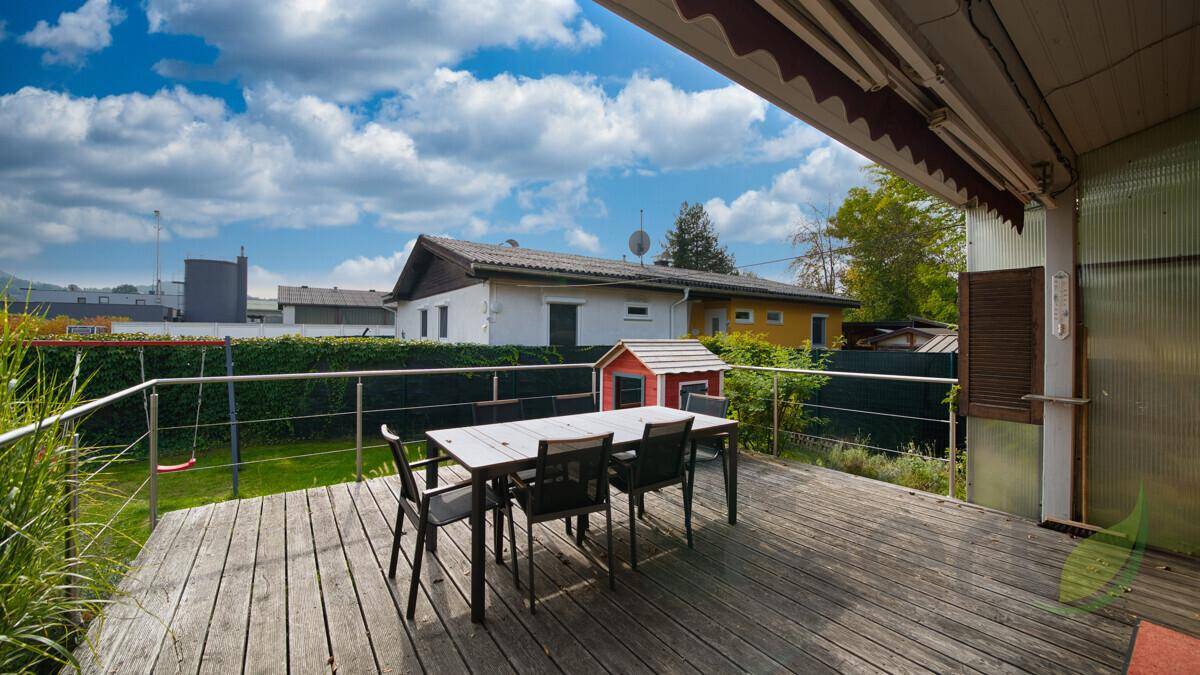 Geräumige Holzterrasse mit Esstisch und Blick auf den Garten und die Umgebung.